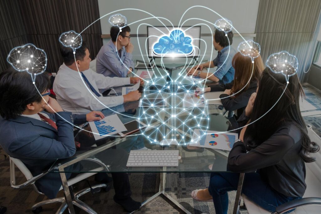 A group of professionals sitting at a conference table with a cloud symbolizing connectivity above the