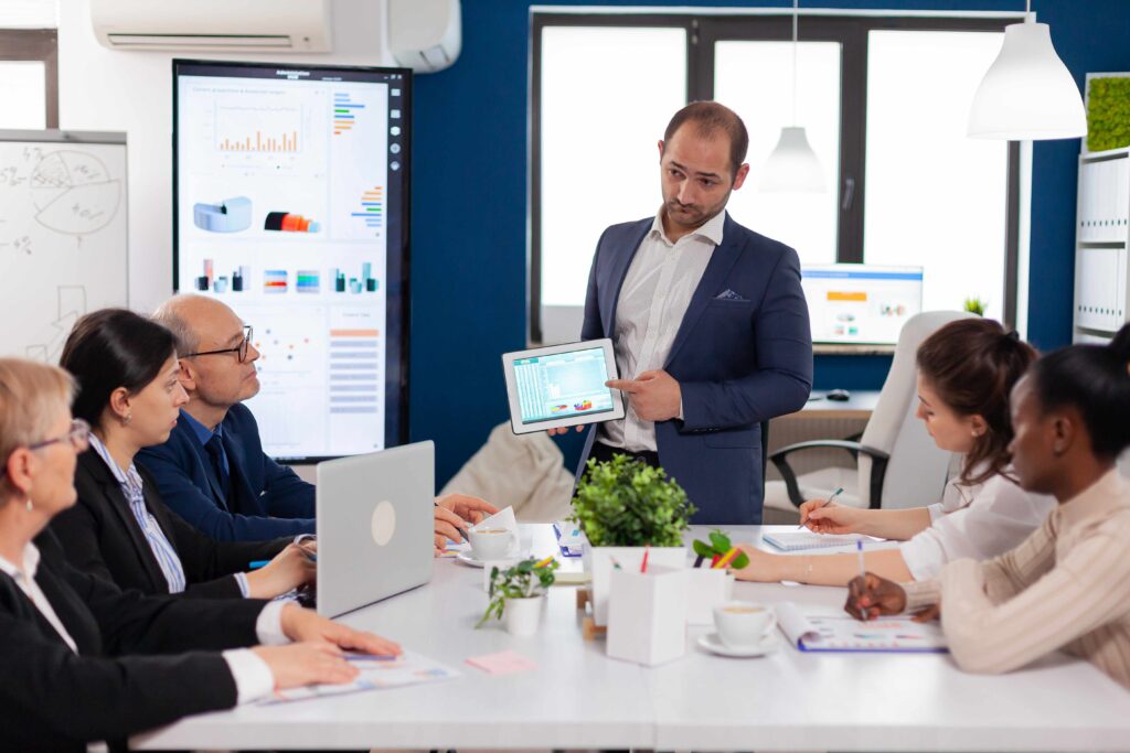 A man presenting to a group of people in a meeting room, emphasizing the importance of efficient resource allocation through managed services in today's competitive business environment.