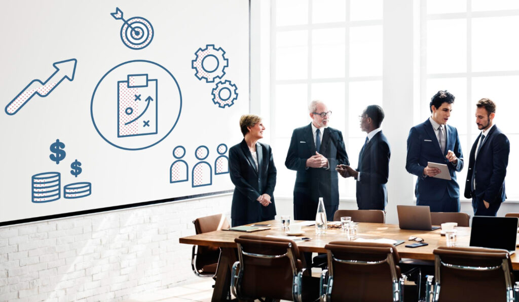 A group of professionals discussing Patch Management Best Practices around a table with a whiteboard displaying icons