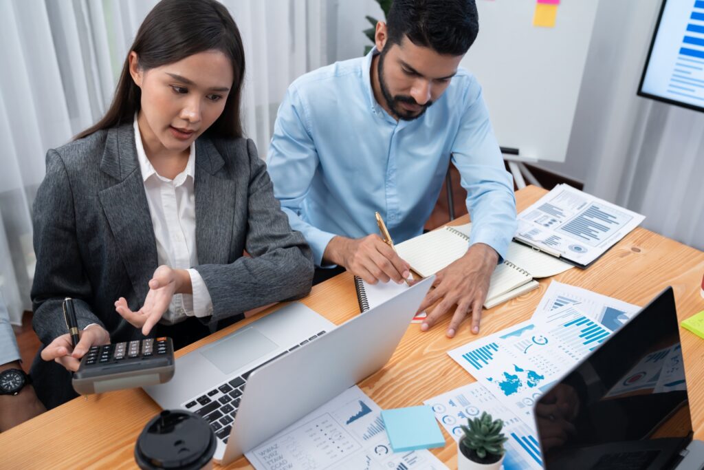 Two professionals collaborating on work using a laptop and documents