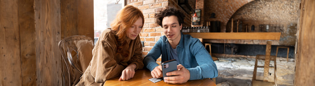 A man and woman sitting at a table, looking at a cell phone together. in dating apps