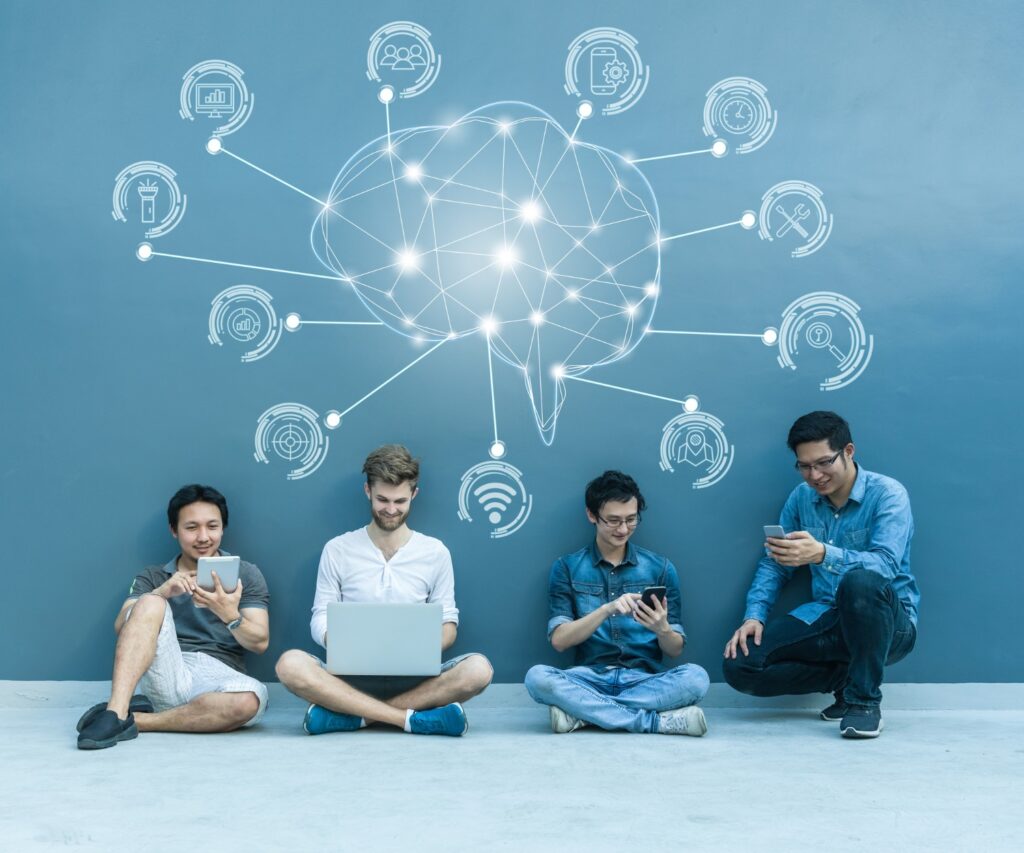 Four young people sitting on the floor with laptops, brainstorming together.