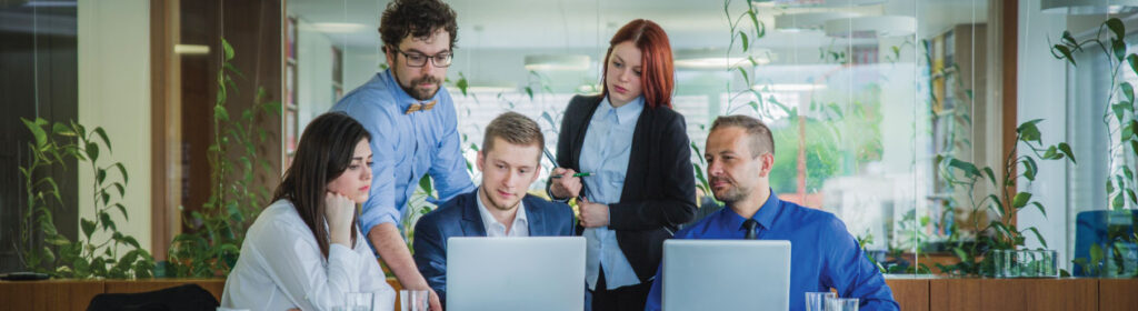 A diverse group of professionals sitting at a table with laptops, engaged in a meeting or collaboration session