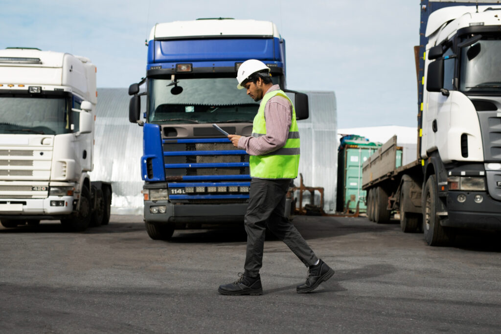 A worker in a hard hat and safety vest walking ahead of a line of trucks at a construction site.