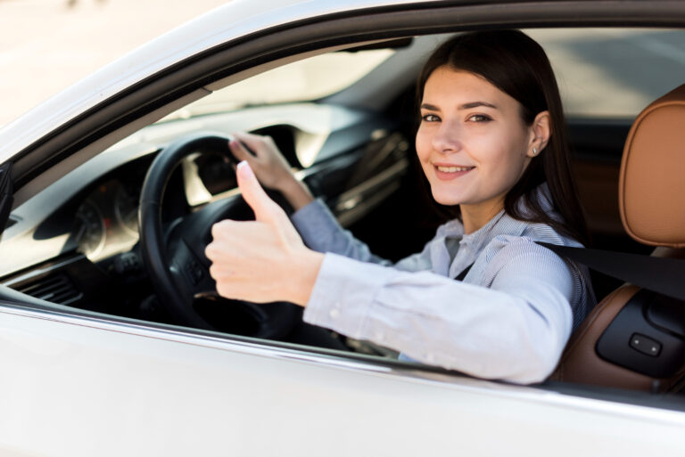 Smiling woman behind the wheel, giving a thumbs up sign.